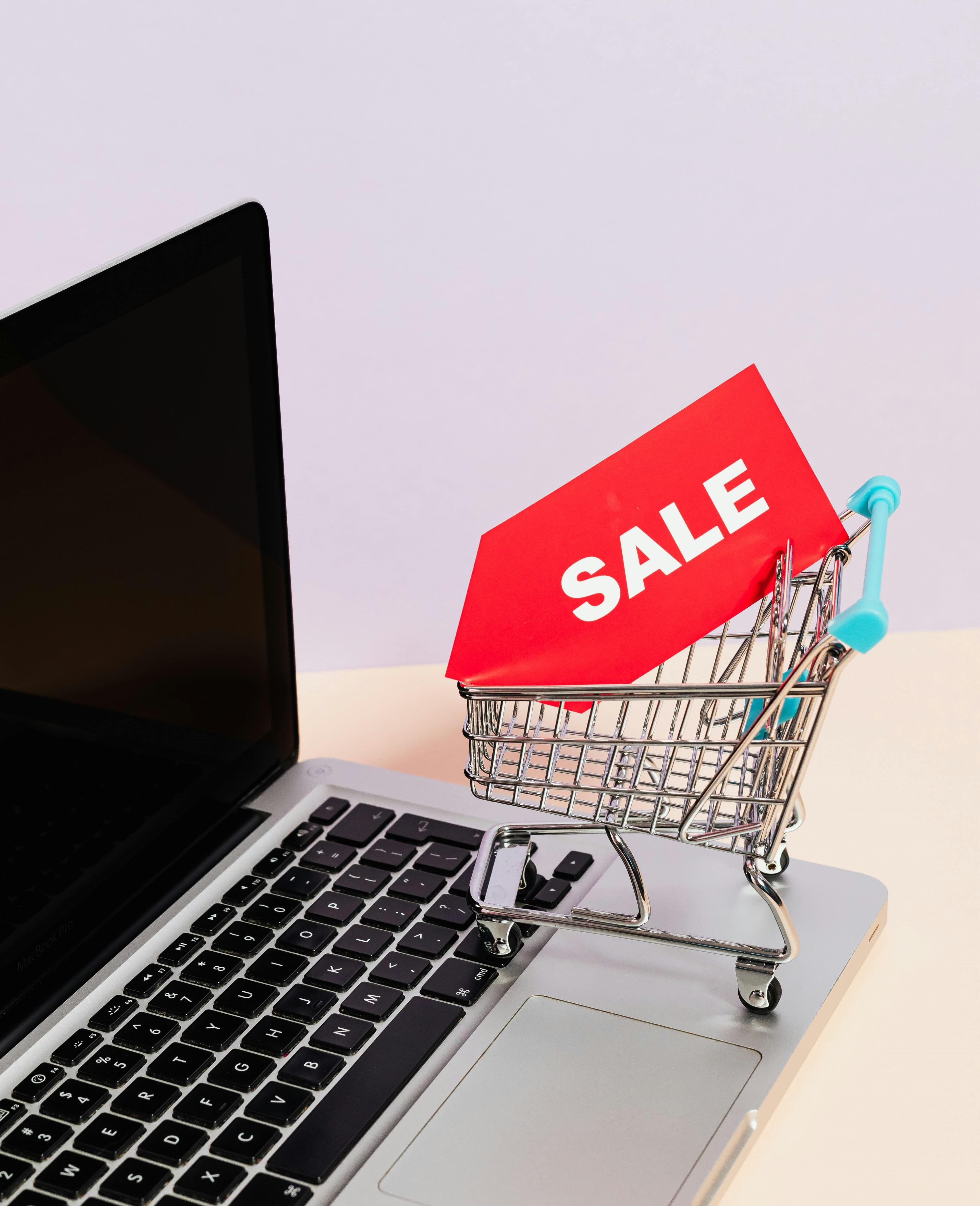 A Red Sale Tag on a Miniature Shopping Cart Placed on a Macbook Laptop