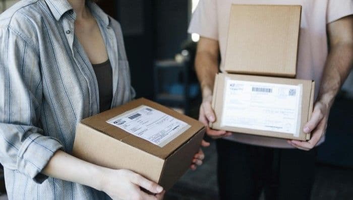 Two people carrying shipping boxes with labels
